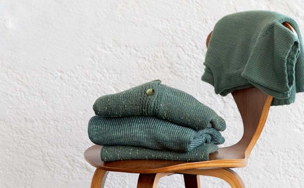 jacken und pullover aus merinowolle in unterschiedlichen gruentoenen auf holzstuhl